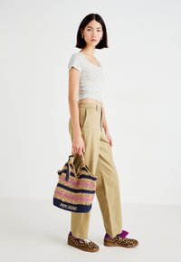 Grå cropped top, beige brede bukser og en multicolor vævet taske med "PEPE JEANS" tekst. Brune sneakers med leopardprint og lilla detaljer.
