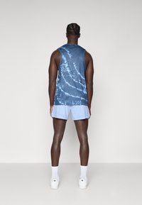 Blå tie-dye ærmeløs skjorte med rund hals. Kombineret med lyseblå sportsshorts og hvide sneakers. Glat stof, afslappet pasform.