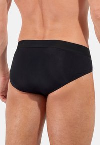 Zwarte zwemslips van een gladde, rekbare stof. Heeft een eenvoudige uitstraling met een comfortabele tailleband en minimale stikdetails.