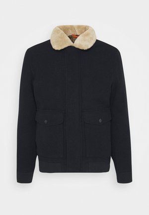 Sort uldjakke med beige kunstpelskrave, to frontlommer med klap og knapper samt ribstrikkede manchetter og kant.