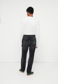 Schwarze Denim-Jeans mit lockerer Passform, ausgestattet mit einem Knopf- und Gürtelschlaufenbund sowie zwei Gesäßtaschen. Getragen mit einem langärmligen weißen Hemd.