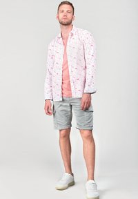 Witte shirt met een patroon van roze flamingo's, gecombineerd met een roze T-shirt, grijze cargo shorts en witte sneakers. Gladde texturen; casual ontwerp.