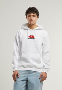 Vit huvtröja i bomull med en känguruficka, prydd med en röd björnlogo och texten "CALIFORNIA" broderad på framsidan.