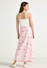 Roze maxi-rok met kleine, verspreide bloemenpatronen. Heeft een luchtige stof en een elastische tailleband. Gecombineerd met een eenvoudig wit topje.
