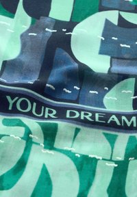 Bavlněná látka s kombinací zelené a modré barvy a výraznými tvary. Text na černém pruhu zní "VAŠE SNY" v stylizovaném písmu.