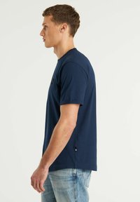 Marinblå bomullströja med korta ärmar, rund halsringning, sidofickor och en liten logotyp på bröstet.