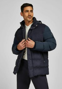 Marine pufferjack met een capuchon, voorzien van een geborduurd ontwerp, ritssluiting en zijzakken, gemaakt van een gladde, matte stof.