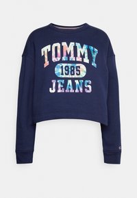 Marinblå kort sweatshirt med långa ärmar. Har "TOMMY 1985 JEANS" i flerfärgad tie-dye-text. Ribbad rundhals och muddar. Mjuk tyg.