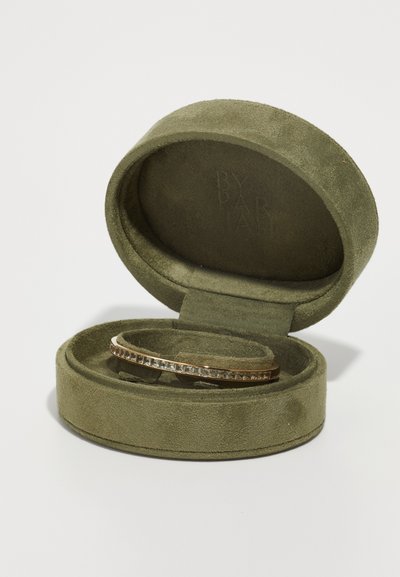 Arany karkötő egy olíva zöld bársonyból készült ékszerdobozban. A karkötő egy sima sávban elhelyezett átlátszó kövek sorával rendelkezik.