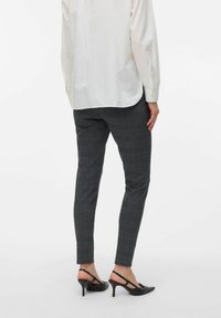 Pantalons à carreaux gris avec une coupe slim, en tissu texturé et accents bleus. Associés à des chaussures à talons hauts noires et une chemise blanche à manches longues.
