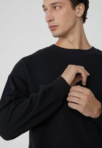 Donkerblauwe sweatshirt met een klassiek ronde hals, verlaagde schouders en ribgebreide manchetten. Soepele textuur en casual pasvorm, met een eenvoudig ontwerp.
