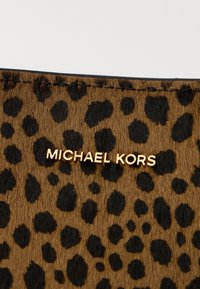 Surface texturée imprimé léopard marron et noir avec lettrage doré "Michael Kors" près du bord cousu.