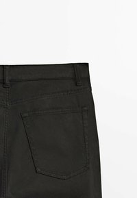 Jean en denim noir montrant la poche arrière, les passants de ceinture et les coutures sur un fond blanc.