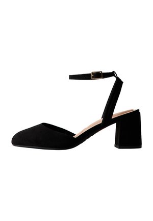 Zapato de mujer de tacón bloque en ante negro, con punta puntiaguda y correa en el tobillo con una pequeña hebilla dorada.