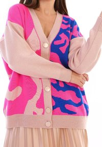 Stickad cardigan med djärva rosa och blå abstrakta mönster, V-ringad design, oversized passform och stora beige knappar.