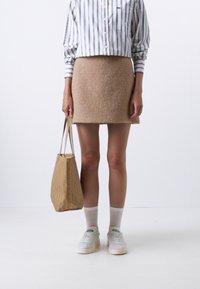 Beige wollen rok, wit en blauwe gestreepte overhemd met knopen, patroon beige totebag, witte sneakers en lichte sokken. Eenvoudige, moderne outfit.