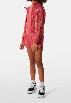 Röd lättviktsjacka med nätpaneler, ihop med en matchande röd topp och shorts. Svart- och vitrutiga högskor.