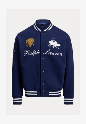 Laivastonsininen collegepusero, jossa valkoiset raidat hihansuuissa ja kauluksessa, kirjailutettuja logoja ja napillinen etumusta. Pehmeä materiaali.