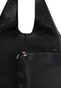 Zwarte leren tas met een gladde textuur, geperforeerd ontwerp en een ritsvak met gouden hardware. Gebogen, brede schouderbanden.