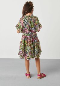 Mnohobarevné šaty s volánkovým lemem a rukávy, s potiskem divokých zvířat v růžové, zelené a černé barvě. Nohou je doplněno o růžové sandály.