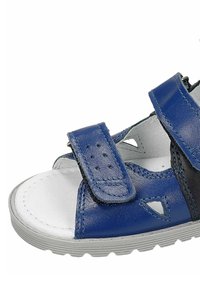 Modré kožené sandály s pásky na suchý zip, perforovanými detaily a bílou vnitřní podšívkou. Šedá gumová podrážka s texturovaným designem.