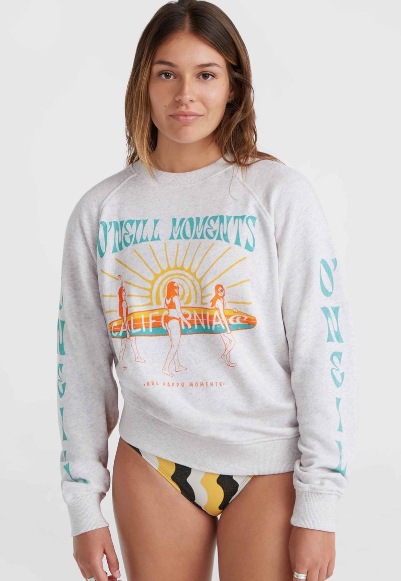 Felpa grigia con una grafica colorata che raffigura surfisti e testo. Maniche lunghe con accenti turchesi. Abbinata a un bikini a fantasia nera e gialla.
