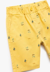 Pantalones cortos amarillos hechos de algodón con cintura elástica. Presenta un patrón de pequeños veleros, palmeras y olas.