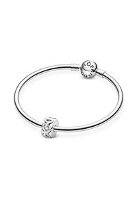 Pulsera de plata con un diseño de alambre circular y suave. Presenta un charm texturizado con un nudo y una cuenta redonda con letras grabadas.