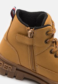 Rudi zomšos batai iki kulkšnies su šoniniu užtrauktuku, tekstūruota pamušalu, sustiprintu siūlių siuvimu ir spalvingomis raištelėmis. Savybė - ryškus prekės ženklas ant guminiu pado.