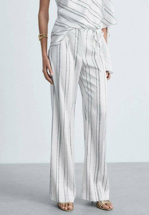 Pantalons larges blancs avec des rayures verticales noires, dotés d'une ceinture à nouer et d'une texture lisse, associés à un haut fluide et des sandales à lanières.