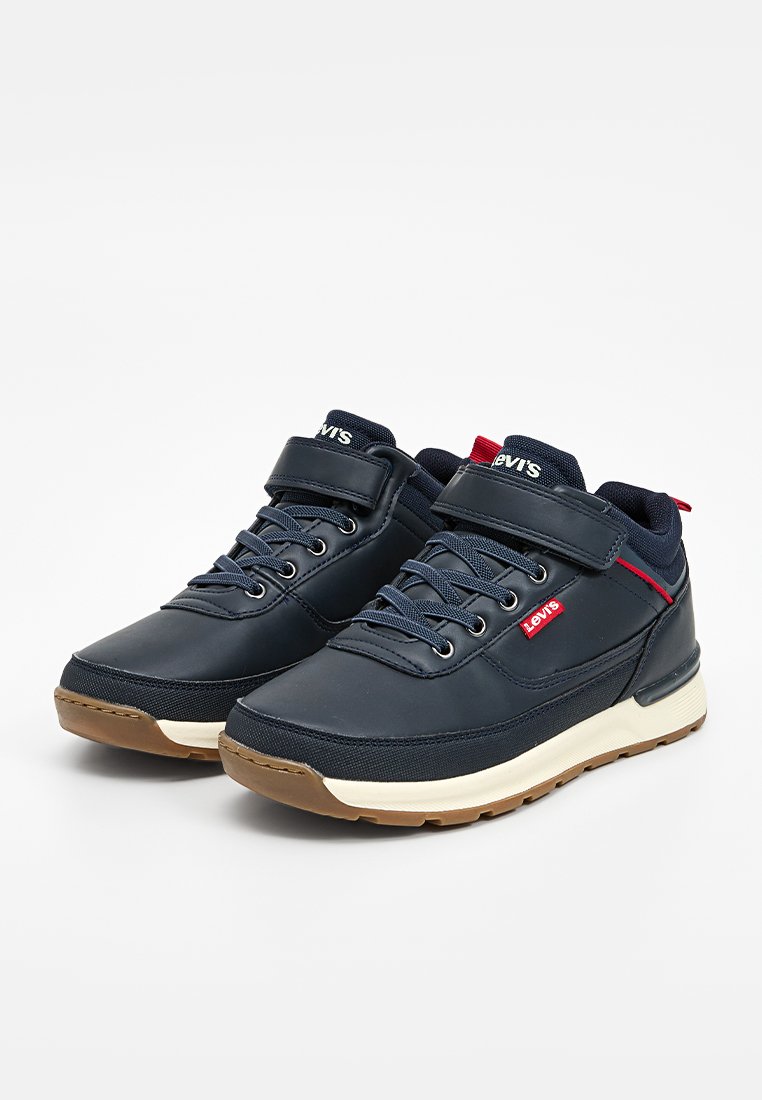 Zapatillas deportivas de color azul marino con una parte superior suave, cierre de cordones, correa ajustable y suela de goma. Presentan acentos de marca en rojo y blanco.
