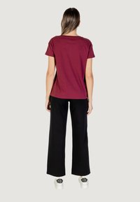 T-shirt di cotone bordeaux con maniche corte, abbinato a pantaloni neri a gamba larga e sneakers bianche. Design semplice con vestibilità rilassata.