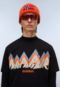 T-shirt preta com um gráfico colorido de montanha em laranja, azul e bege, acompanhada de um gorro de malha laranja com a bandeira da Noruega.