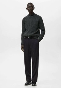 Maglione a coste grigio scuro abbinato a pantaloni scuri a vita alta, completato da una cintura nera e scarpe nere lucide.