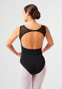 Schwarzer Bügelanzug mit Netzpaneelen, offenem Rückendesign und einem modischen Schnitt. Kombiniert mit hellrosa Strumpfhosen wirkt der Stoff glatt und elastisch.