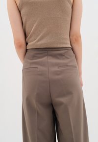Pantaloni marroni a zampa d'elefante con una texture liscia, dotati di due tasche posteriori e una vita alta, abbinati a un top in bronzo.