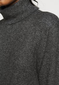 Mörkgrå polotröja i mjuk, texturerad stickad tyg. Har hög krage och lös passform med subtila fläckar.