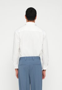 Weißes Langarmhemd und blaue Hose mit Nadelstreifen. Das Hemd hat einen klassischen Kragen, und die Hose ist mit Gesäßtaschen und Gürtelschlaufen ausgestattet.