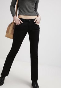 Jeans neri in denim a zampa d'elefante con vita media, tasche anteriori e una texture liscia. Abbinati a un top grigio a coste e una borsa beige.