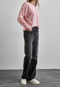 Jasnoróżowa bluzka z długim rękawem i okrągłym dekoltem, zestawiona z czarnymi, wysokim stanem jeansami. Całość dopełniają białe trampki.