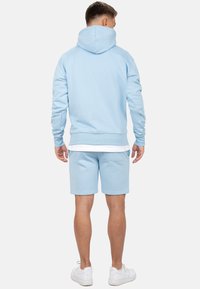 Haut de survêtement bleu clair avec capuche à cordon, poignets côtelés et shorts assortis. Tissu lisse avec une coupe décontractée ; présente une poche arrière.