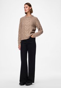 Beiger, gestrickter Pullover mit Zopfmuster, Rundhalsausschnitt und langen Ärmeln, kombiniert mit schwarzen, hoch taillierten Schlagjeans und schwarzen Schuhen.