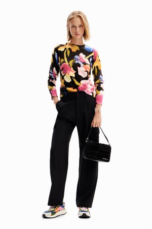 Maglione lavorato a maglia con un motivo floreale colorato su sfondo nero, abbinato a pantaloni neri, una borsa nera e sneaker multicolori.