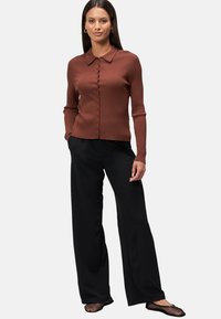 Rostfarbener, gerippter Langarm-Cardigan mit Kragen und Knopfverschluss, kombiniert mit schwarzen weitem Hosen und schwarzen Netzschuhen.