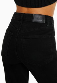 Jeans de denim negros de cintura alta con una textura suave, que presentan una etiqueta de cuero en la parte posterior y dos bolsillos traseros.