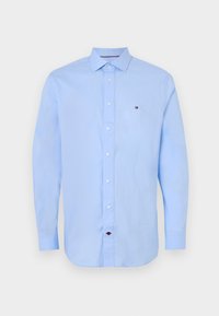 Lyseblå langermet skjorte med krage og knapper foran, hvite knapper og en liten logo-patch på brystet. Glatt stoff og tettsittende passform.