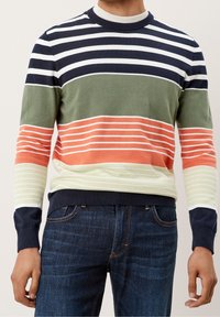 Mann trägt einen mehrfarbigen gestreiften Pullover in Marineblau, Weiß, Grün, Orange und Creme, kombiniert mit dunkelblauen Jeans.