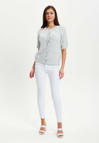 Light gray short-sleeve cardigan in soft, textured fabric with five button front. Paired with white fitted pants and strappy white heels.