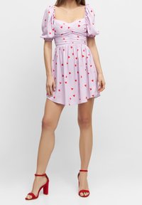 Violetti mekko lyhyillä puffimaisilla hihoilla, rypytetty yläosa, hajaantuneet punaiset sydänkuviot, liehkeä hame; yhdistettynä punaisiin stilettokorkoihin.
