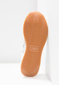 Semelle de chaussure de sport conçue avec un motif en chevrons, composée d'un matériau en caoutchouc brun, avec une surface texturée pour une meilleure adhérence et un logo au centre.